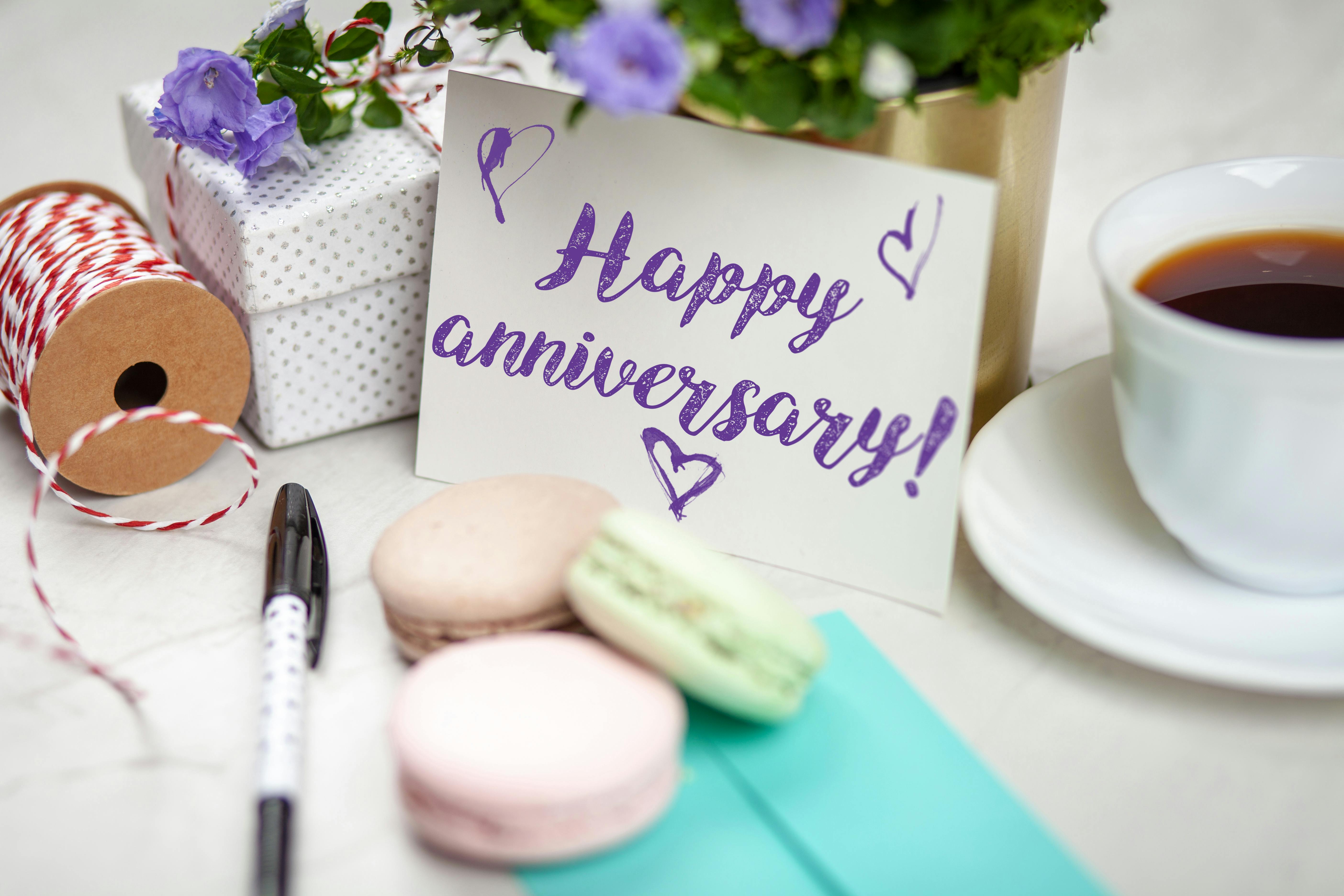 Happy anniversary card with flowers, gift, macarons, and coffee on a table.